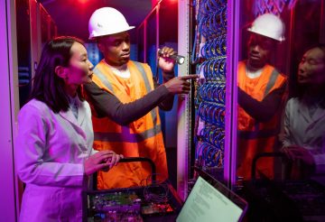 African American workman in hardhat repairing server and explaining reason of server breakdown in data center